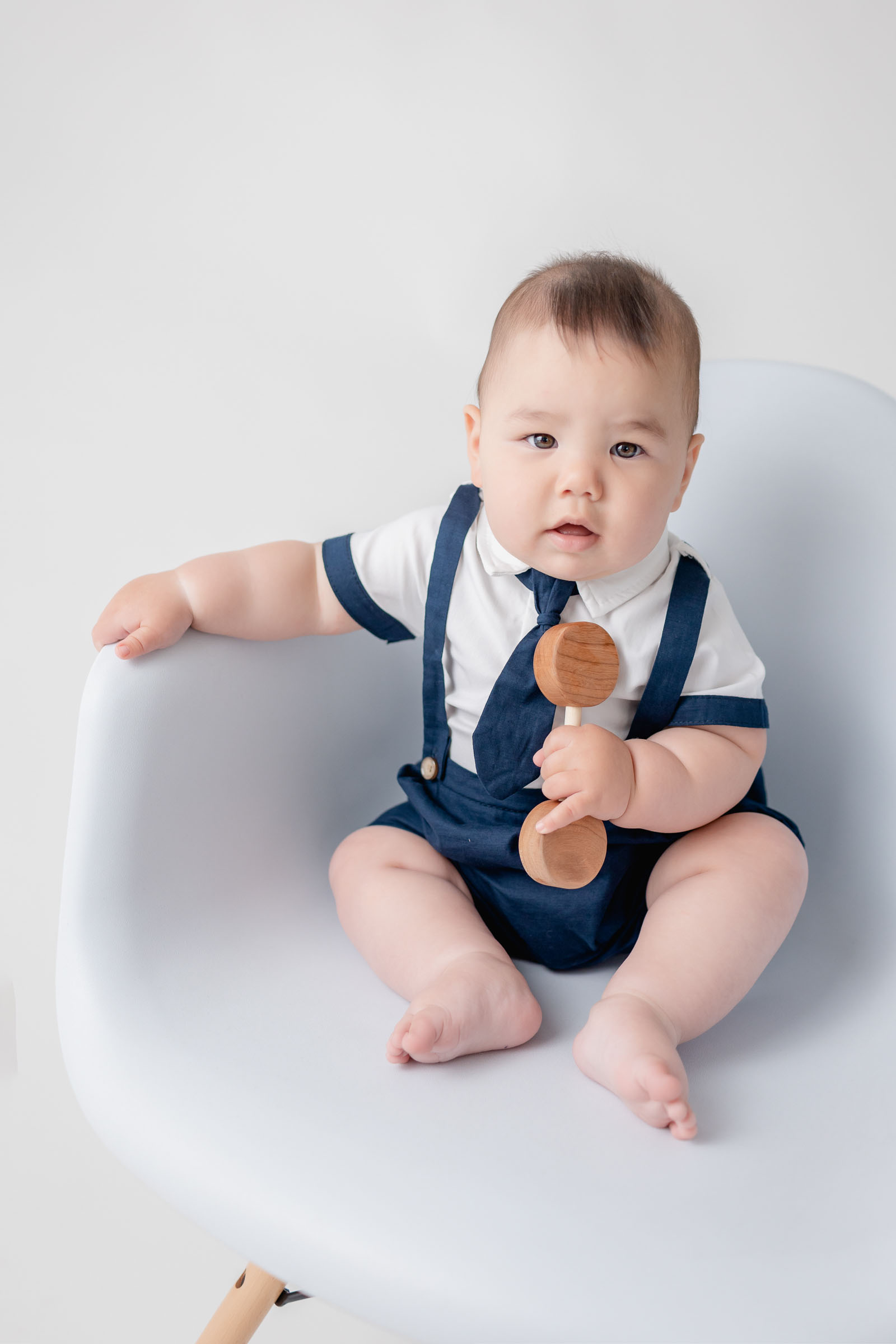 Chunky little baby boy sitting on a white chair for his 6 month sitter photoshoot