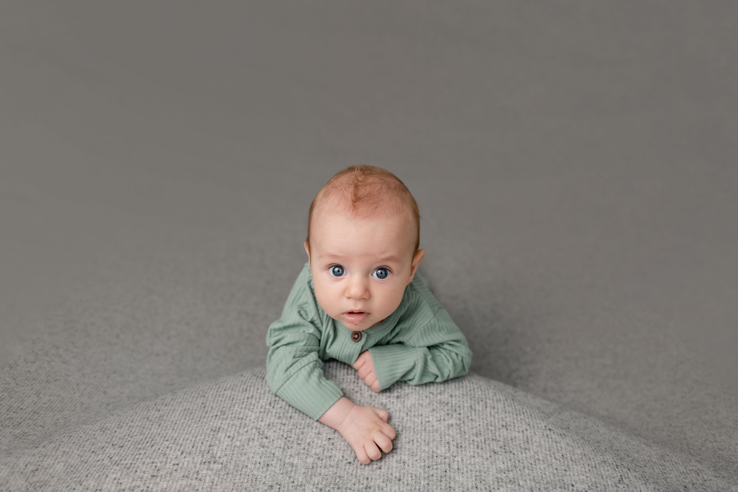 3 month milestone image for baby in green on gray backdrop