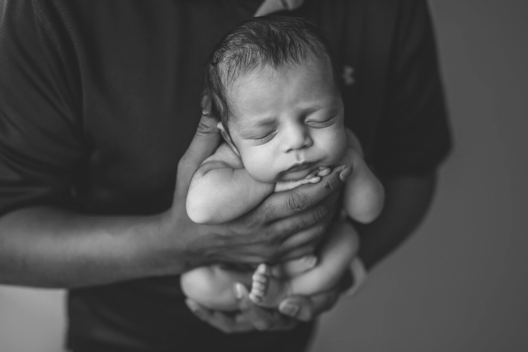 Black and White newborn photograph of dad holding baby in arms