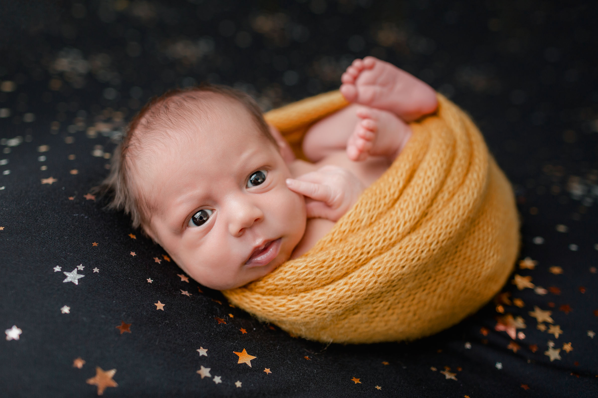 Newborn Session Photo of baby on Black Start Backdrop with Yellow Wrap