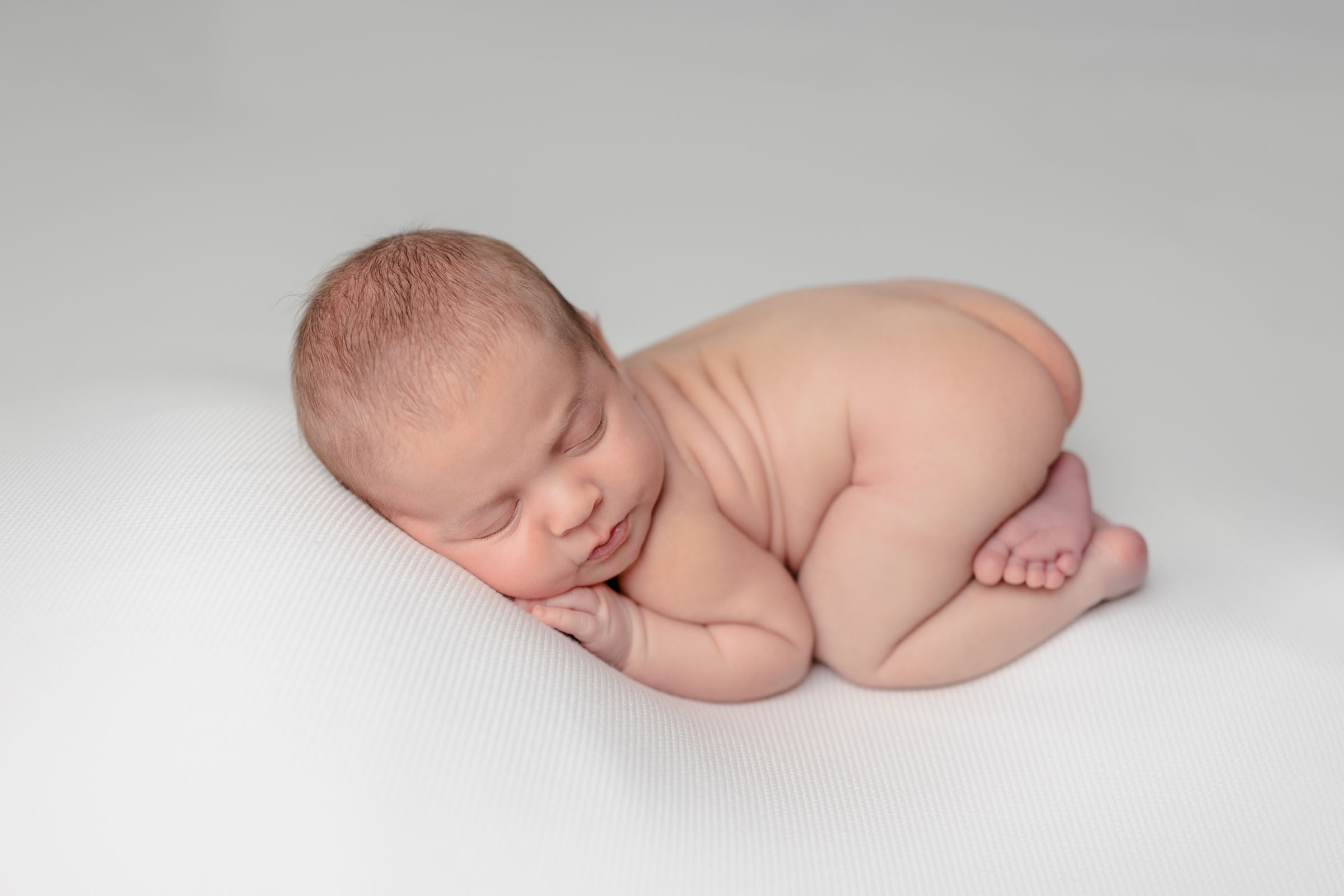 Bum up pose of newborn baby boy on white backdrop