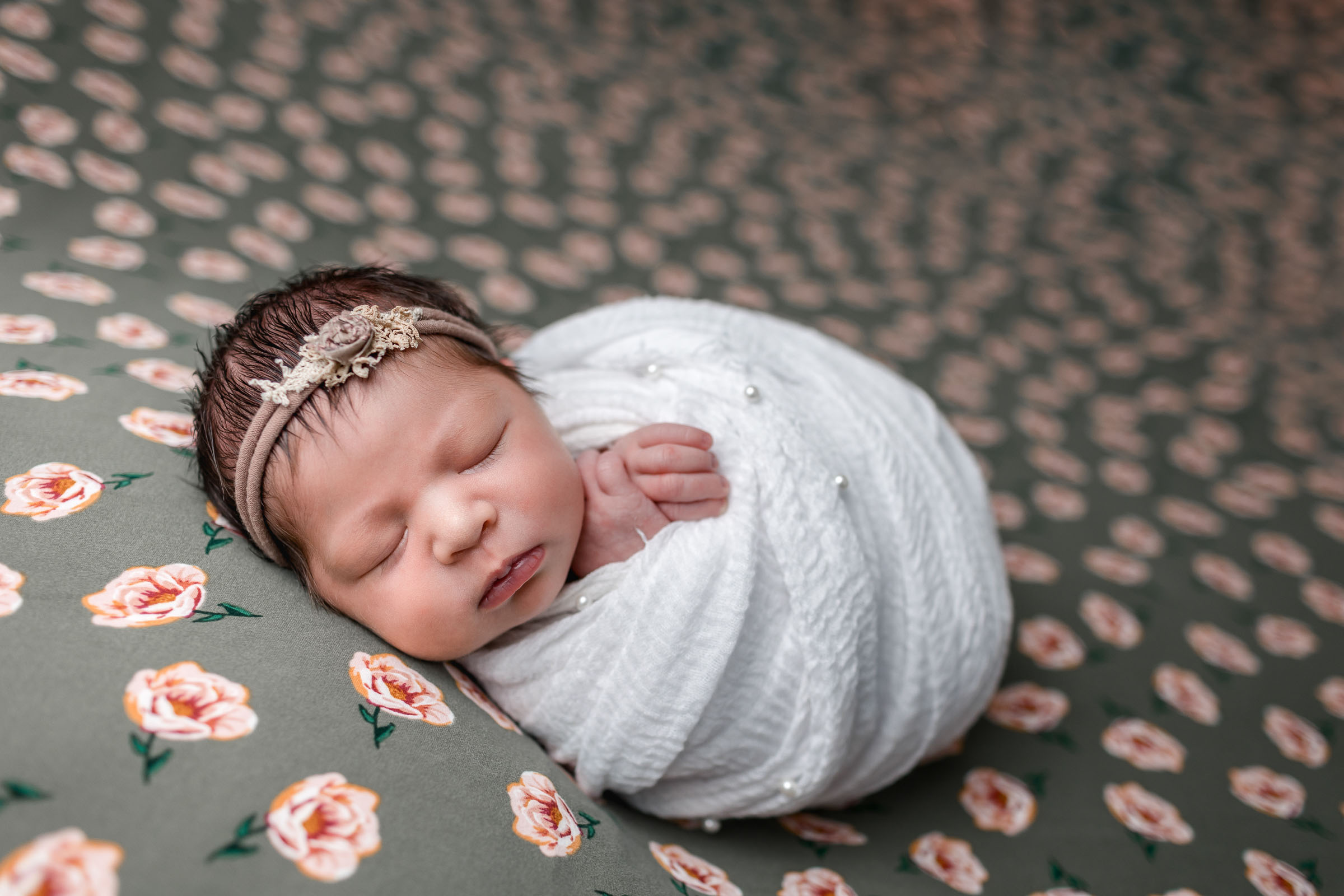 Newborn girl wrapped in white posing on flower backdrop