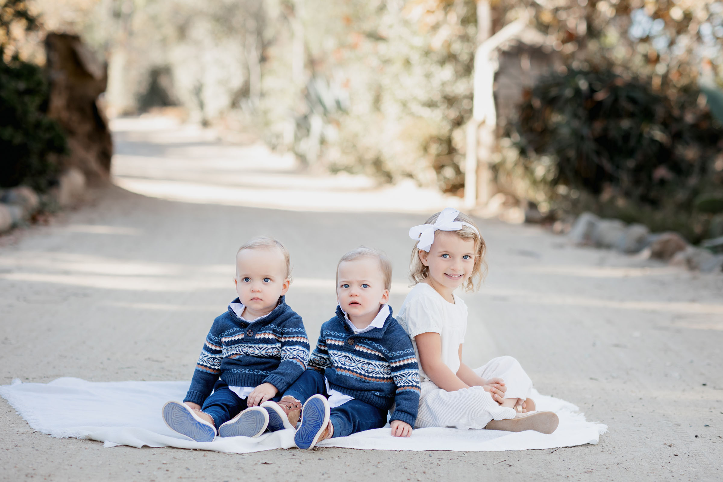 Two twin boys and their big sister sitting on blanker for family pictures in Carlsbad