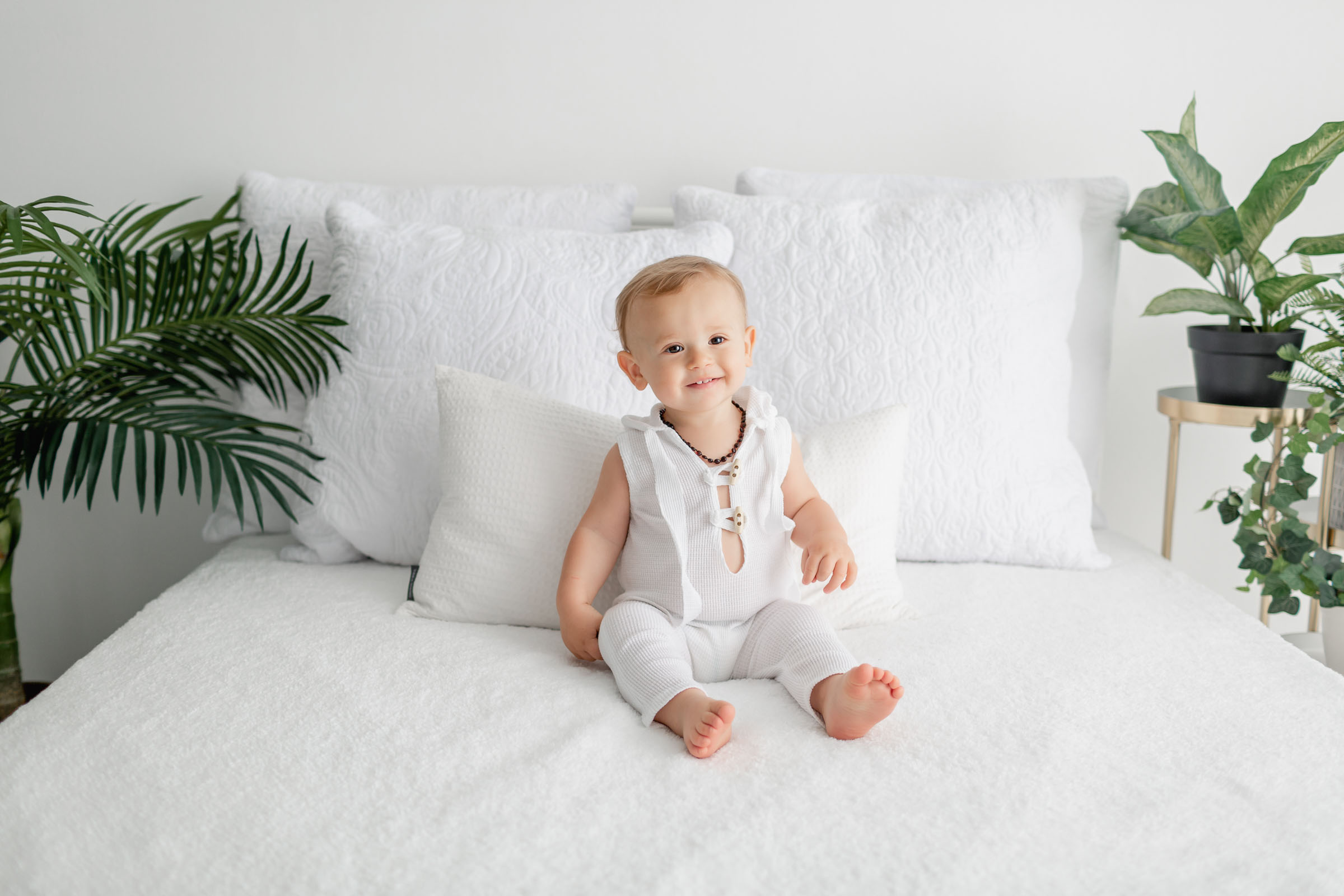 Birthday Boy in white outfit on a white studio bed during his one year pictures