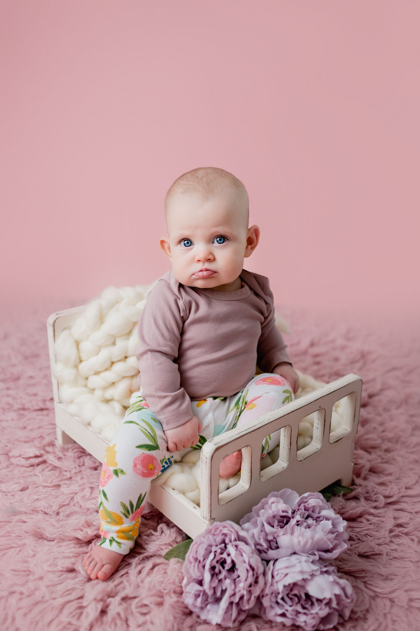Baby girl dressed in pink with flowers on a pink backdrop for her milestone pictures