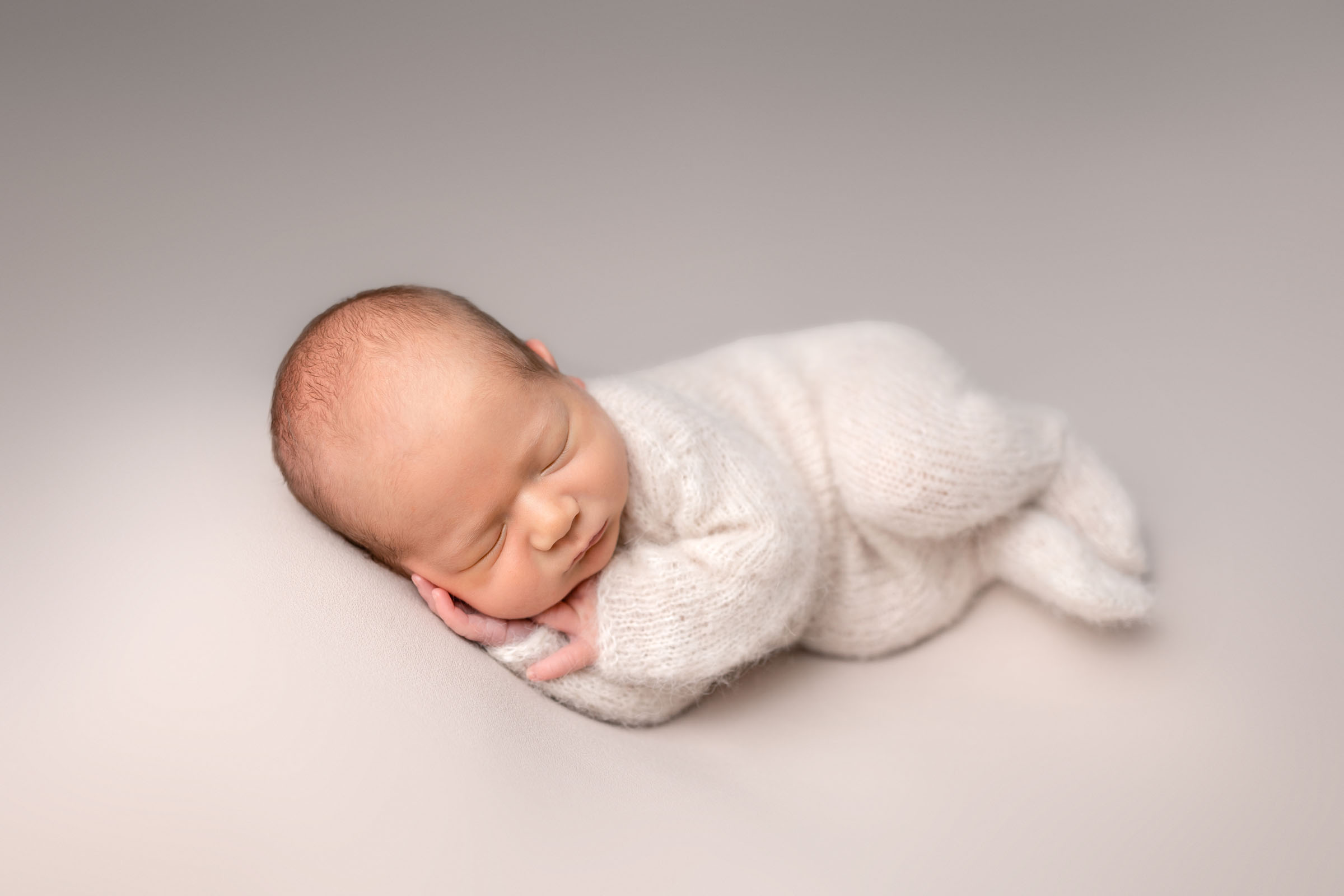 Sweet side laying pose of newborn dressed in neutral outfit on a beige backdrop