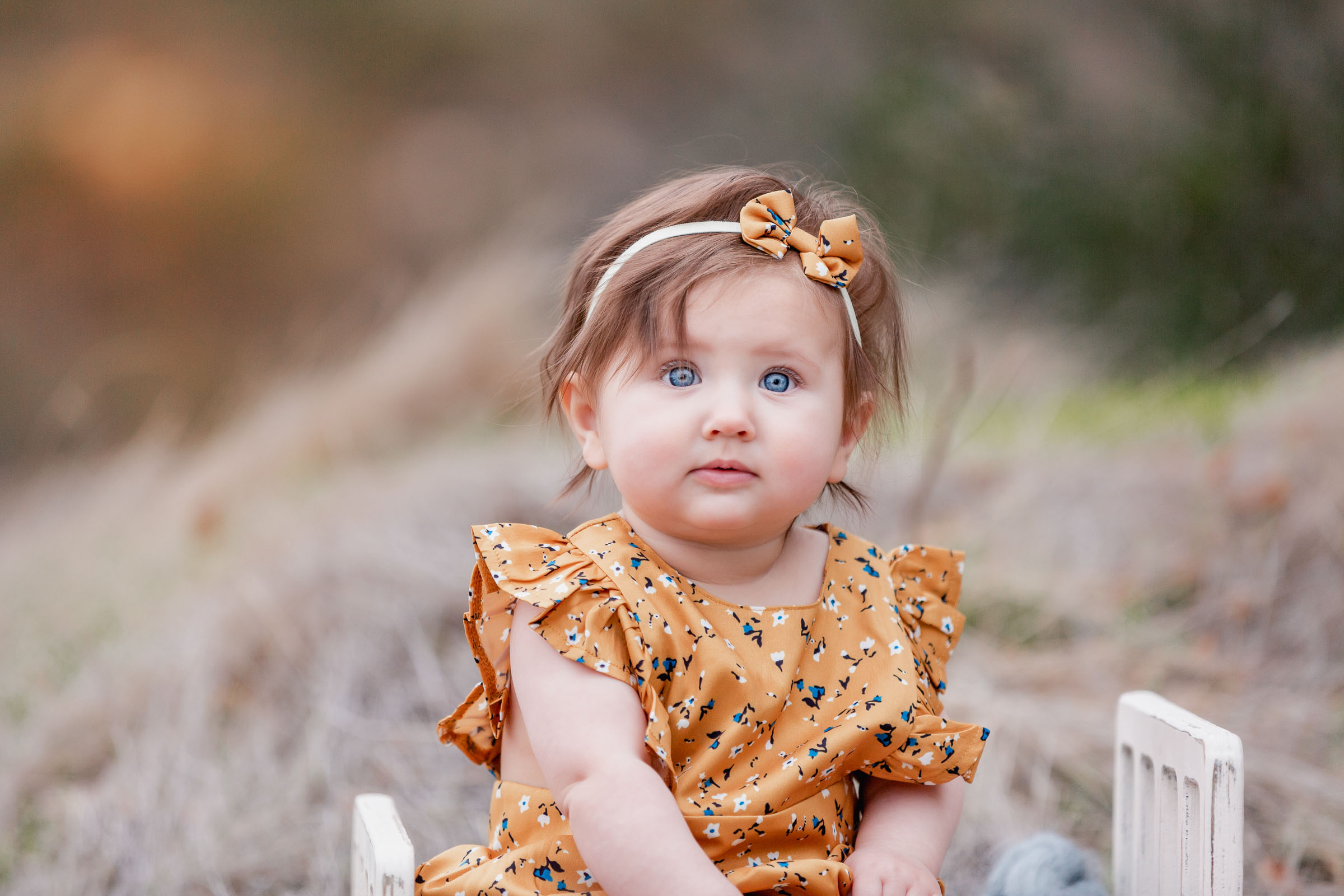 Close up of baby girl during outdoor photoshoot in San Diego dressed in a yellow outfit with small blue flowers