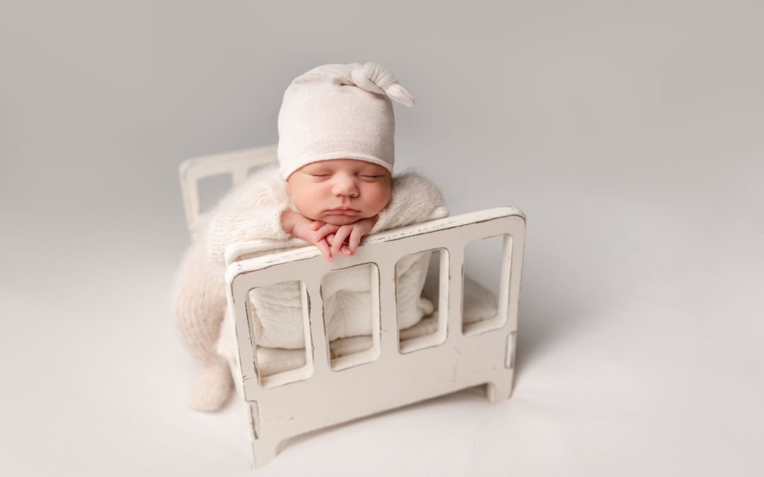 Beautiful Simple Newborn Picture taken during gorgeous Studio Newborn Photos in San Diego of baby in white outfit on a white bed on a white backdrop.
