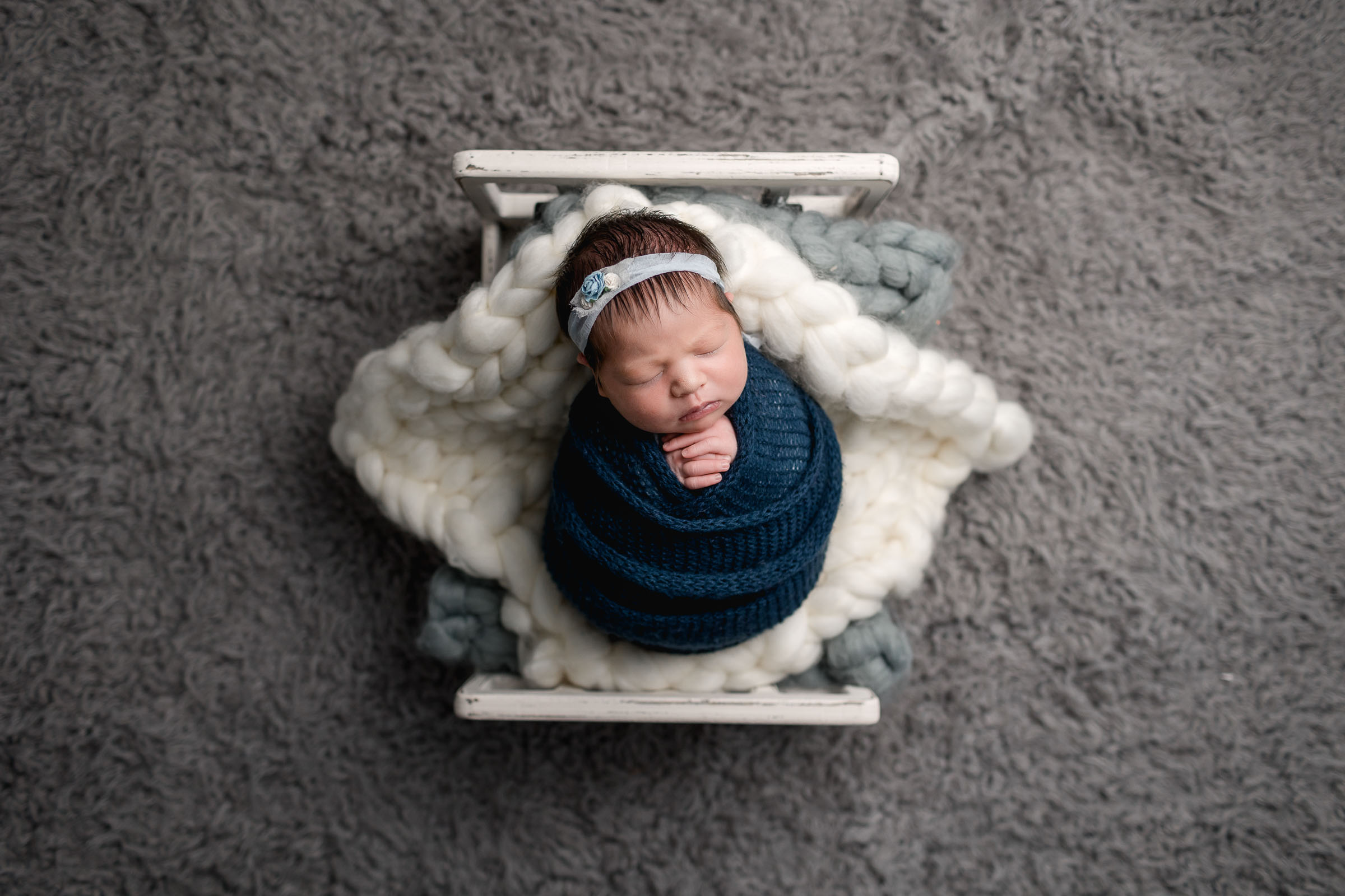Newborn girl wrapped in blue posed on a doll bed on a gray fur rug by San Diego Newborn Photographer