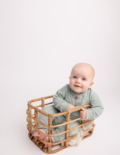 Baby boy sitting in a basket in a mint green outfit during 6 month milestone pictures