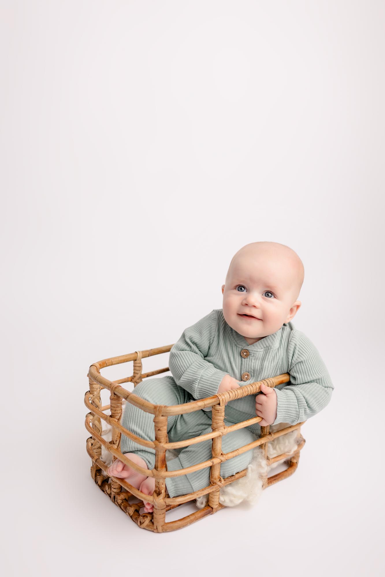 Baby boy sitting in a basket in a mint green outfit during 6 month milestone pictures
