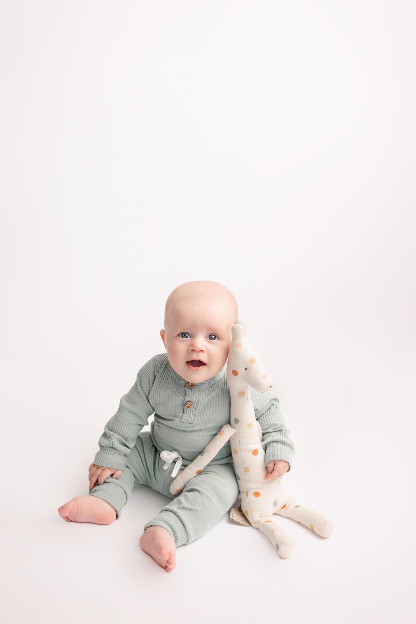 Smiling baby boy in mint green outfit sitting with a giraffe during Milestone Pictures at San Diego Professional Photography Studio