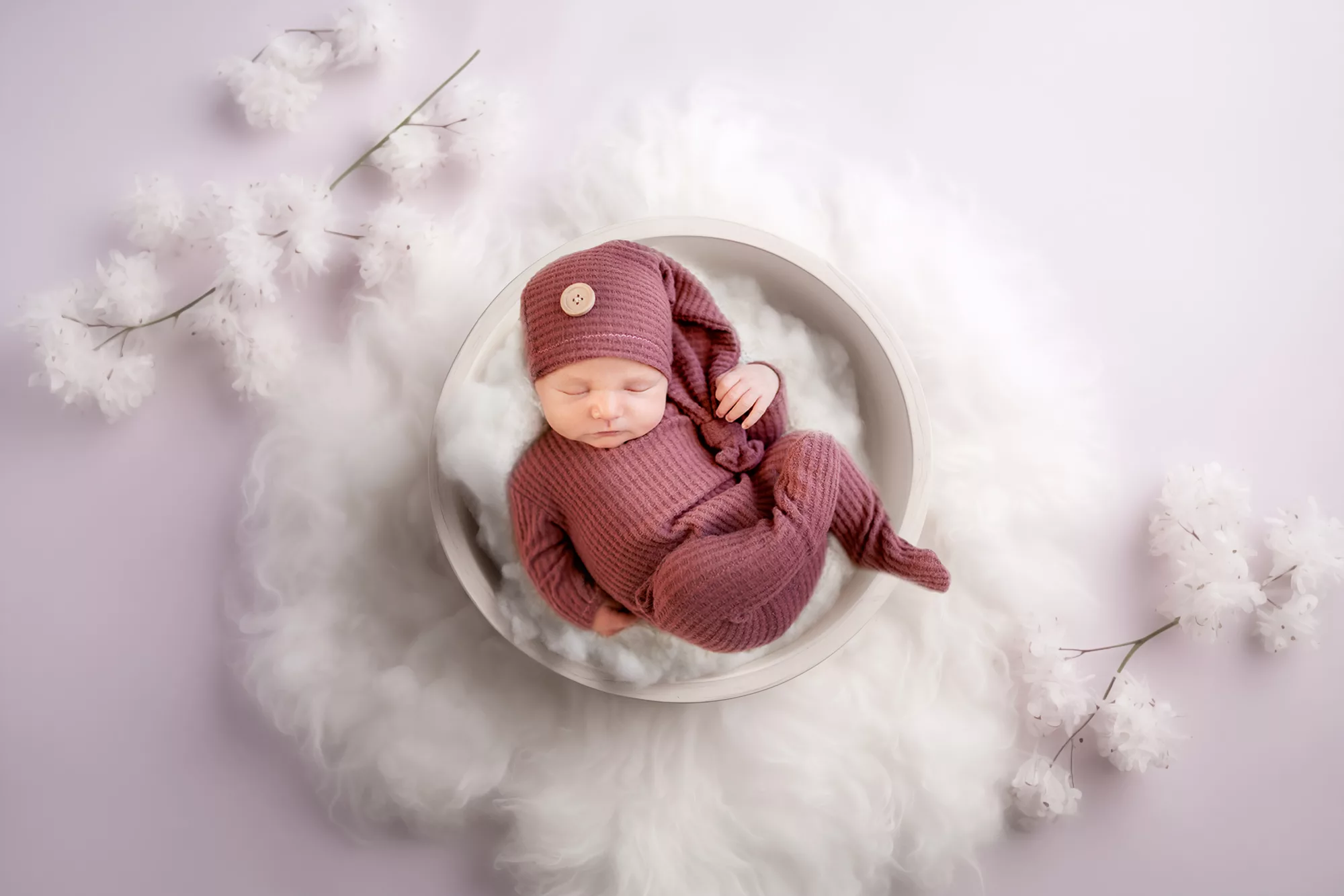 Newborn Girl Photography in a pink outfit laying in a bowl of white fluff on a white rug and pink background