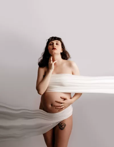 Fine Art Portrait of pregnant mom on a white backdrop featuring a mom covered with chiffon fabric in an artsy display with bare belly