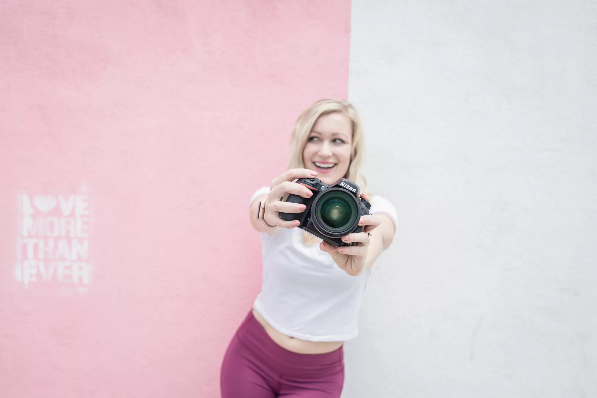 Female Photographer posting against a wall holding our her camera for her branding pictures wondering if she should be tipping her photographer