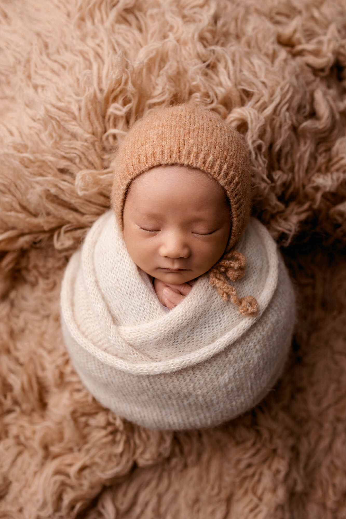 Beautiful Newborn Photos in San Diego of baby wrapped laying on a caramel fur rug with a matching hat