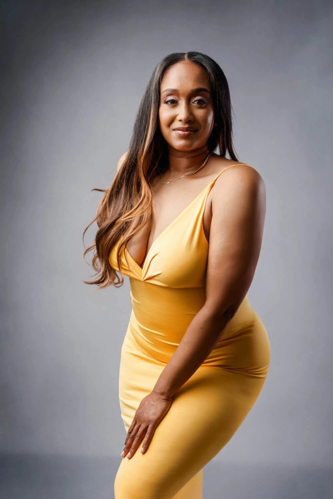 Mother in a fitted amber dress smiling softly, grey studio backdrop