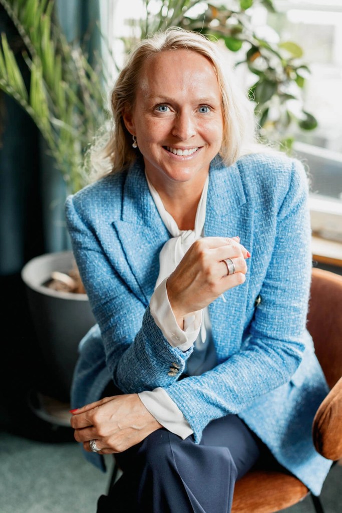 Security consultant in a light blue tweed blazer seated cross-legged near a window and plants