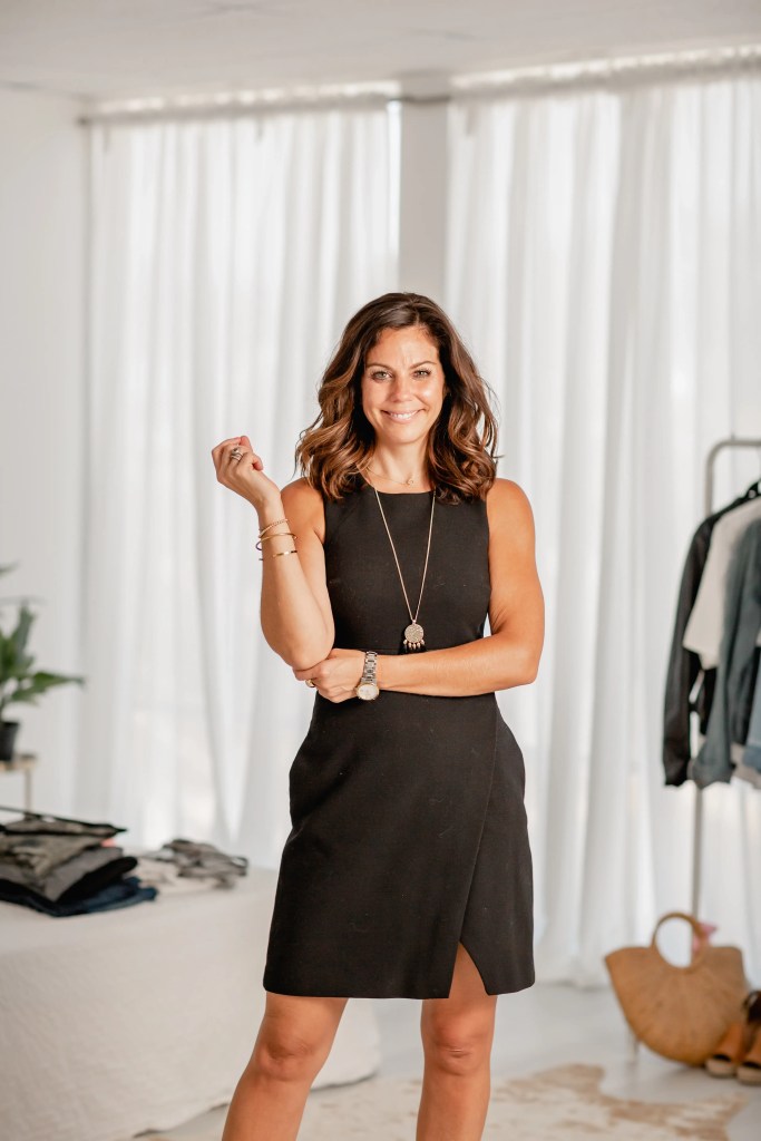 Content creator in a black sleeveless dress, arms crossed, smiling in a bright studio