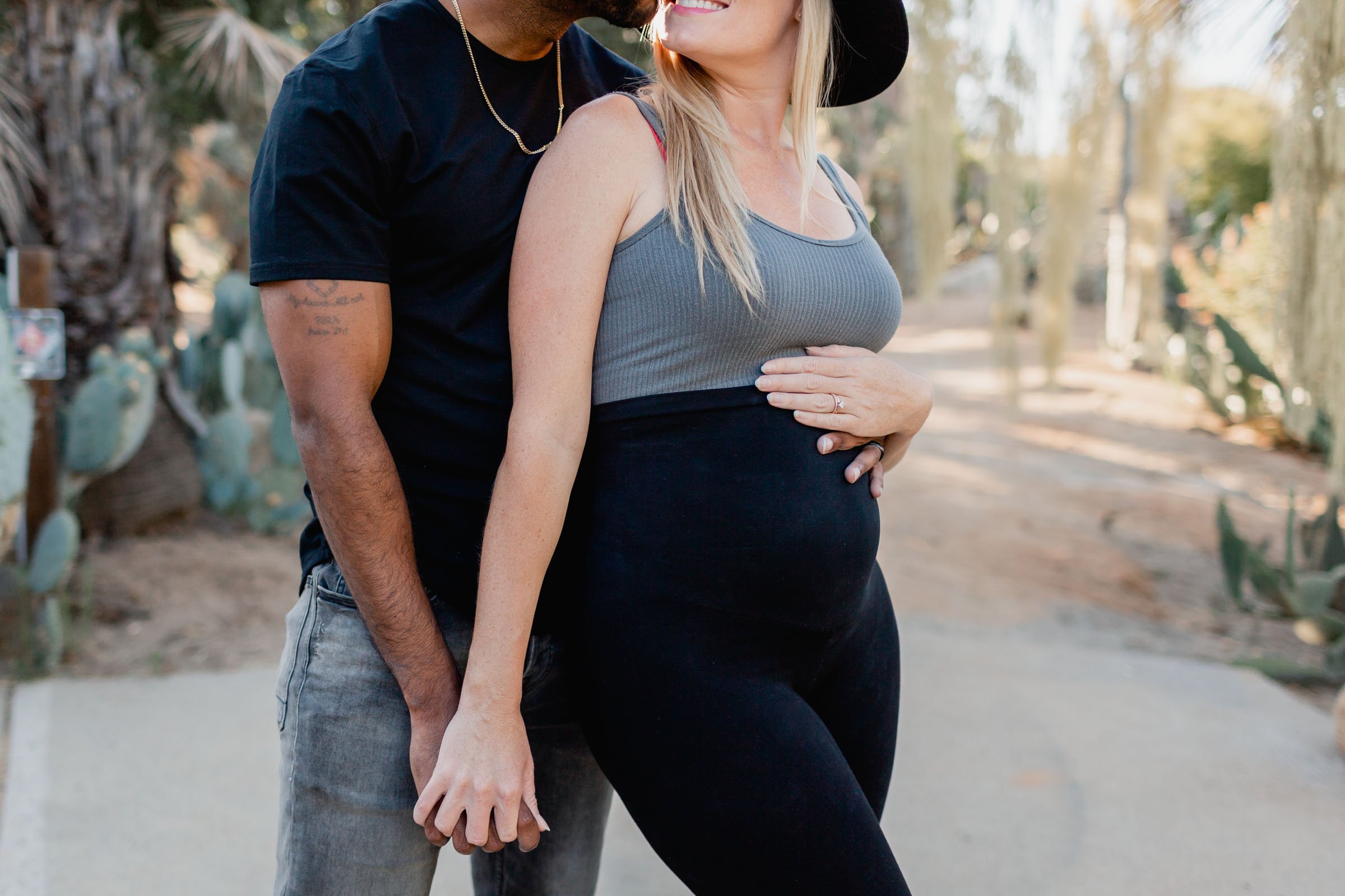 Expectant couple embracing among the cacti of the Balboa Park Desert Garden, her hand resting on her bump
