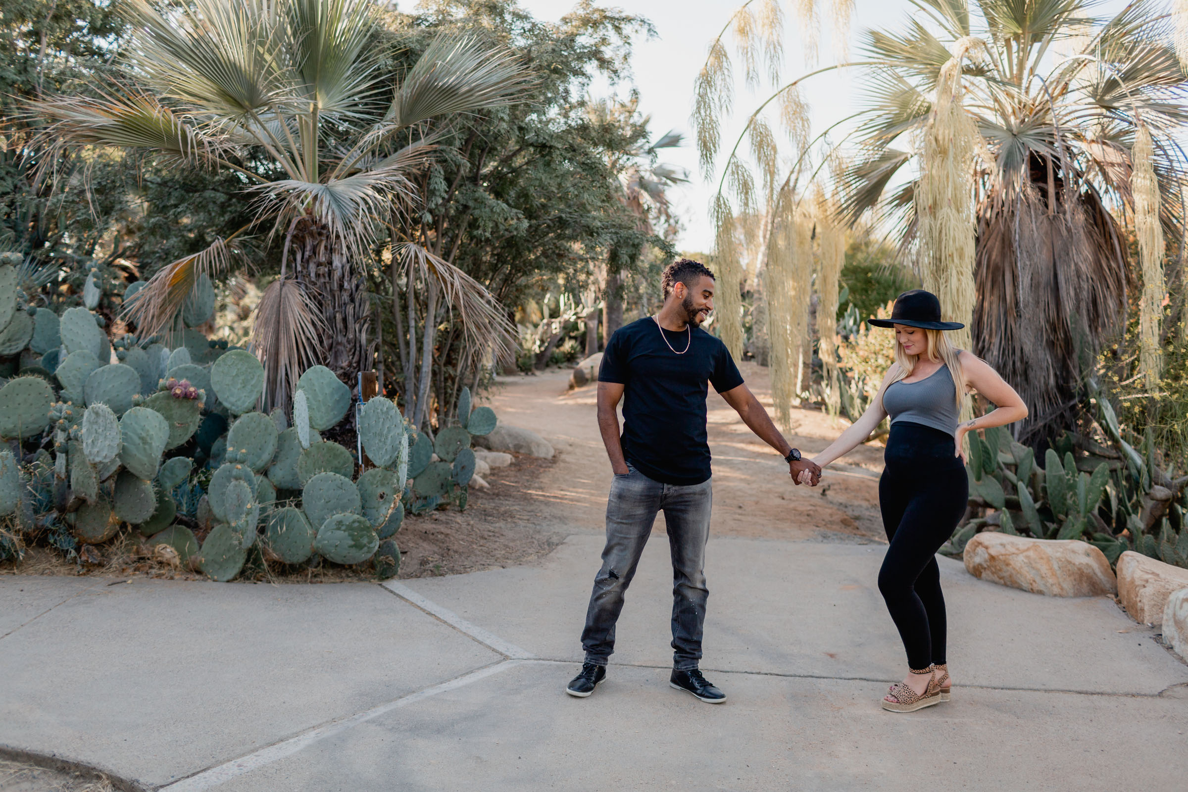 Expectant couple holding hands on a path through the Balboa Park Desert Garden, palms and cacti around them