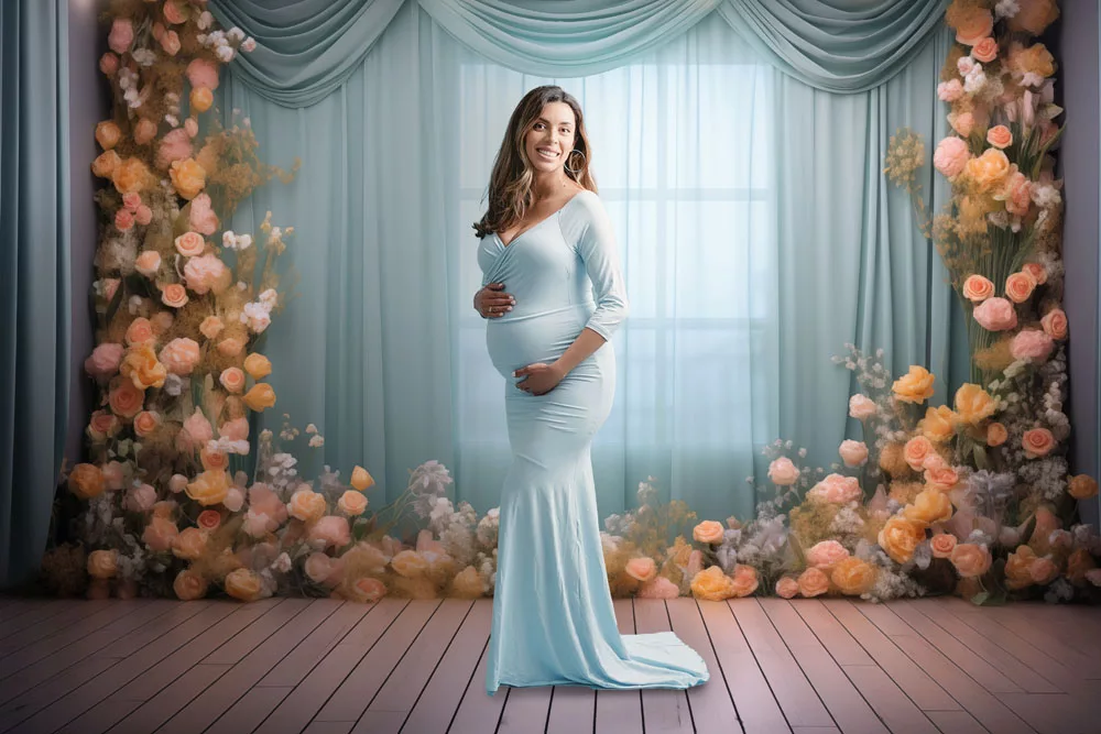 Pregnant woman in a fitted pale blue gown in front of a window framed with peach and pink flowers