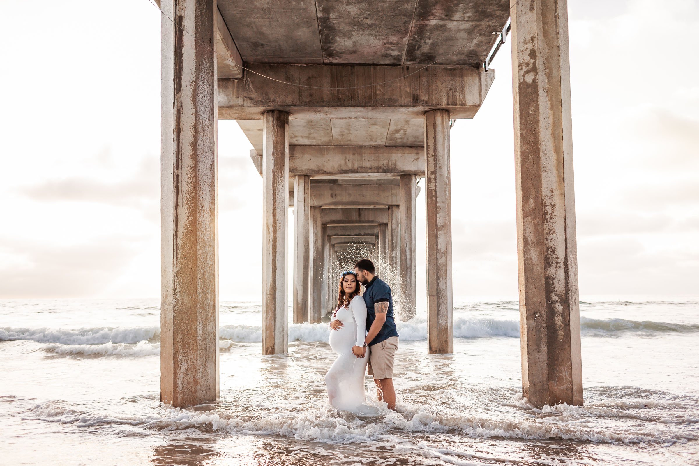 Expectant couple standing in the surf beneath the pillars of Scripps Pier