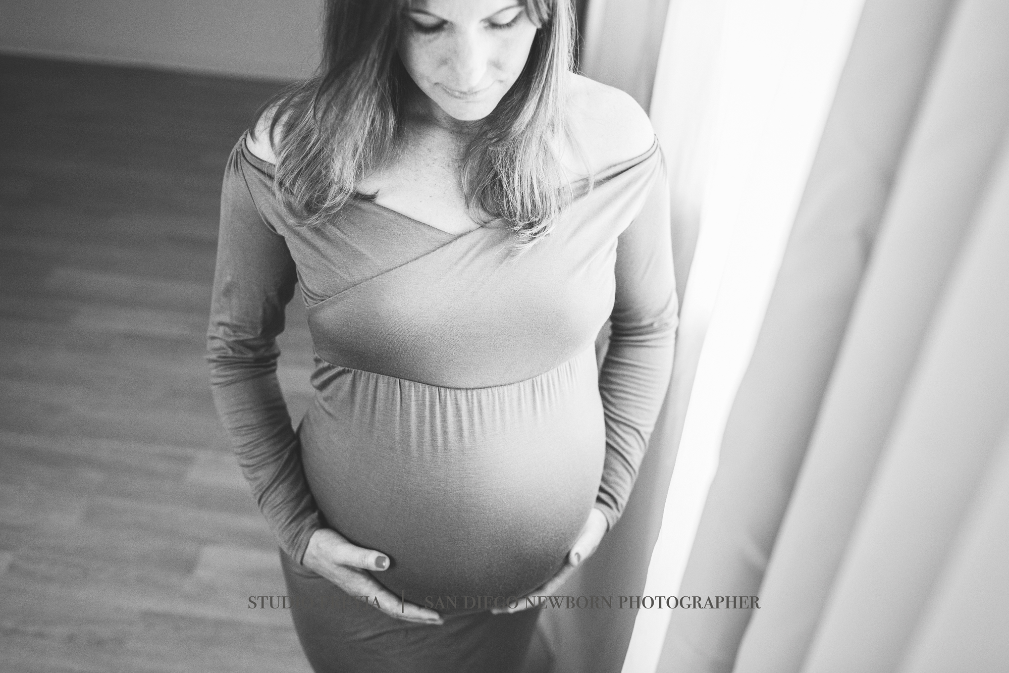Black and white photo of a pregnant woman by a window, looking down at her bump
