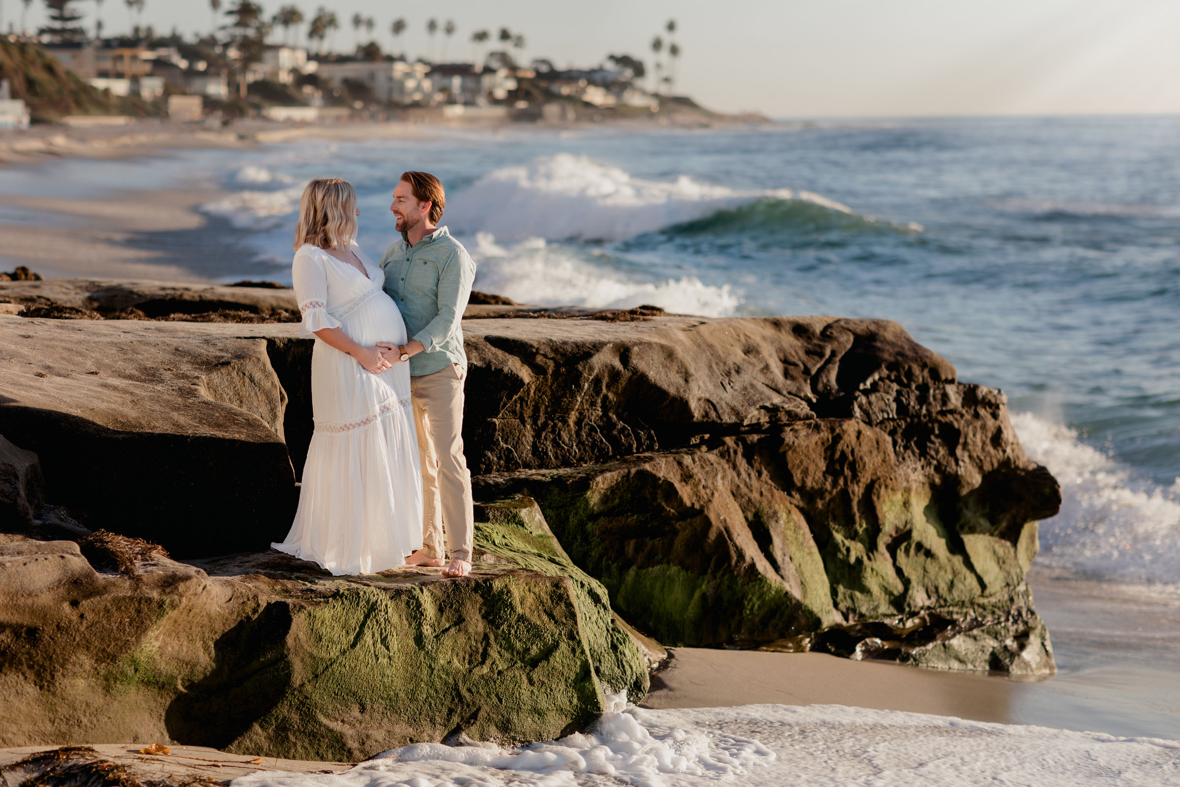Expectant couple standing on a rock at Windansea Beach with waves breaking behind them