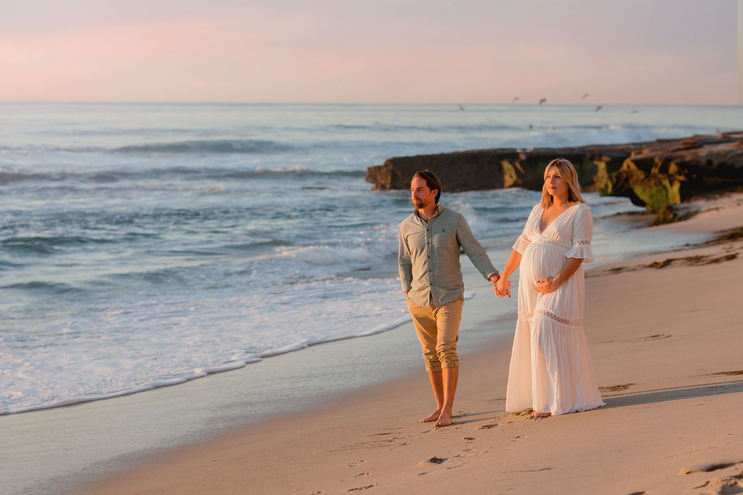 Expectant couple walking hand in hand along the shore at Windansea Beach at sunset