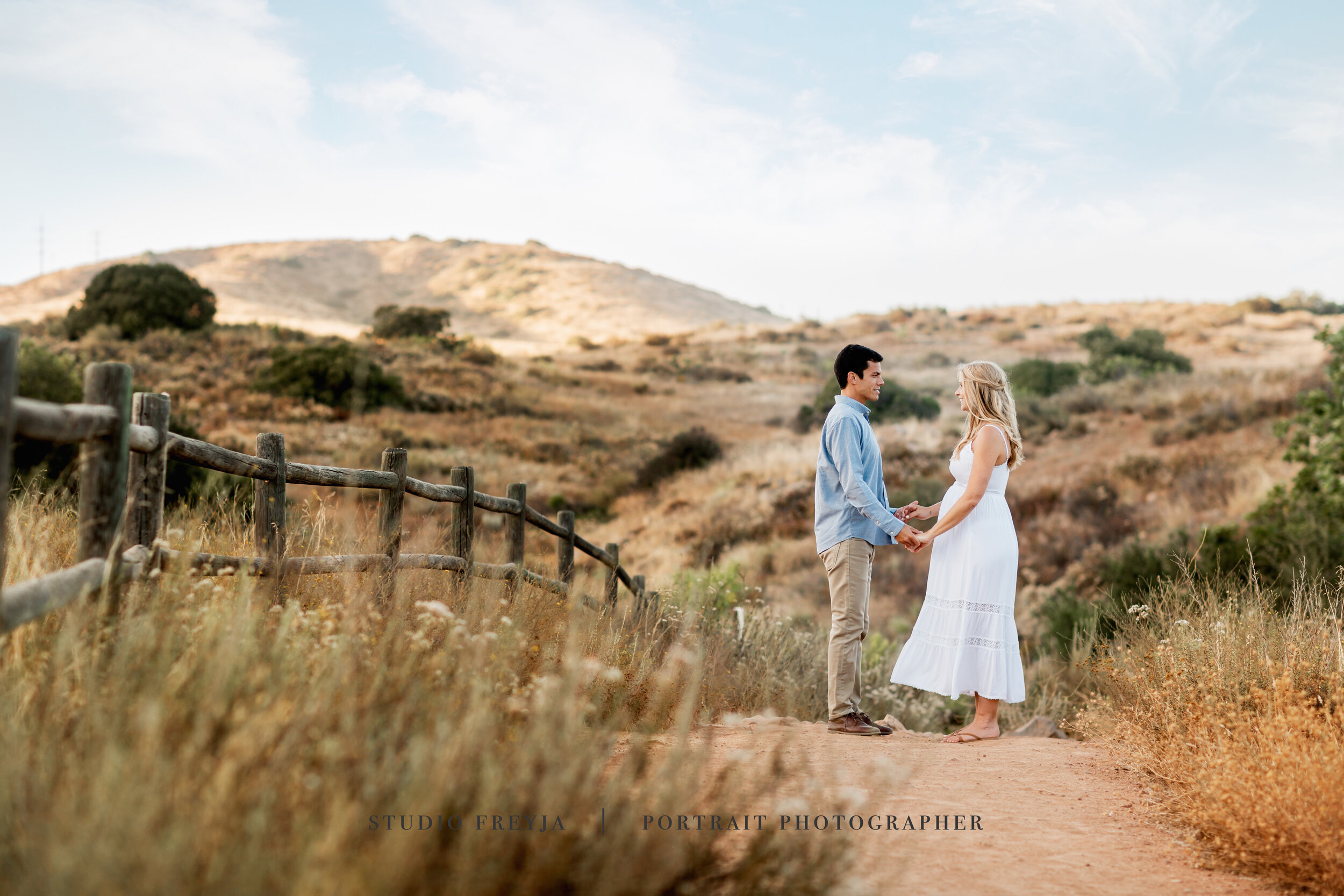 Expectant couple holding hands on a trail through dry golden hills