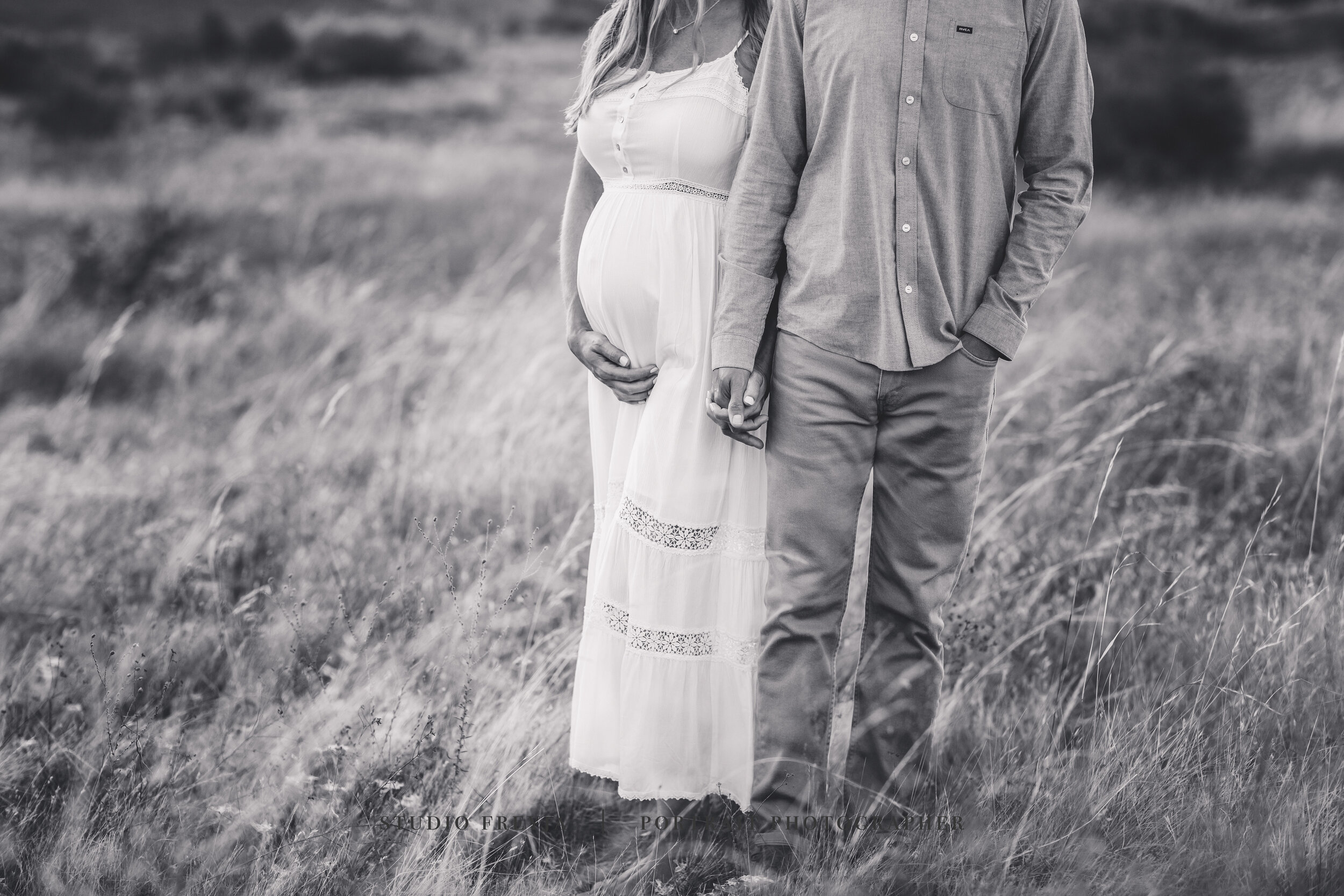 Black and white close-up of an expectant couple standing in tall grass