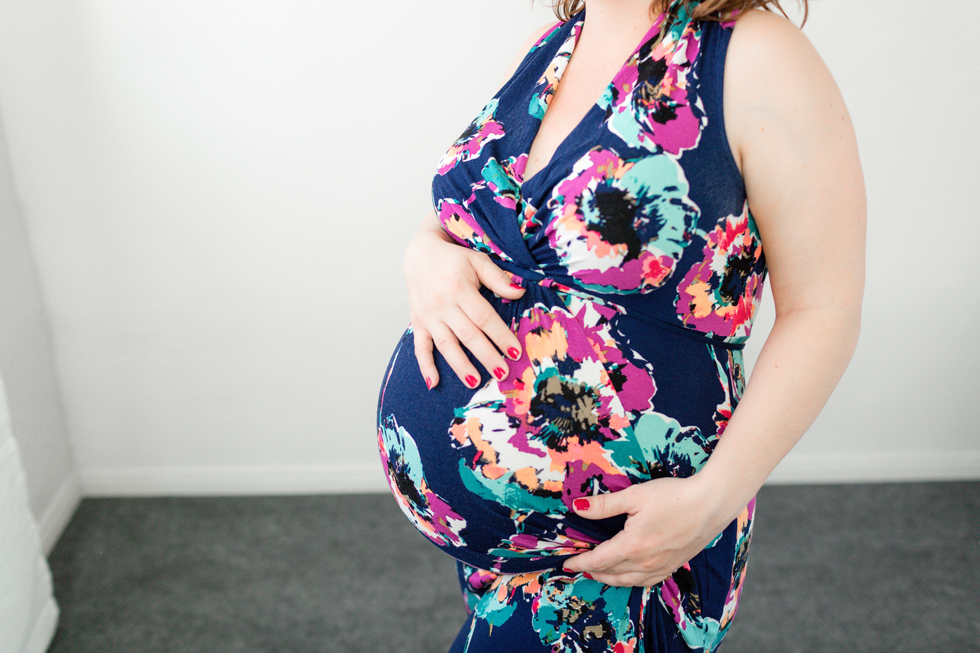 Close-up of a pregnant woman in a bright floral wrap dress cradling her bump