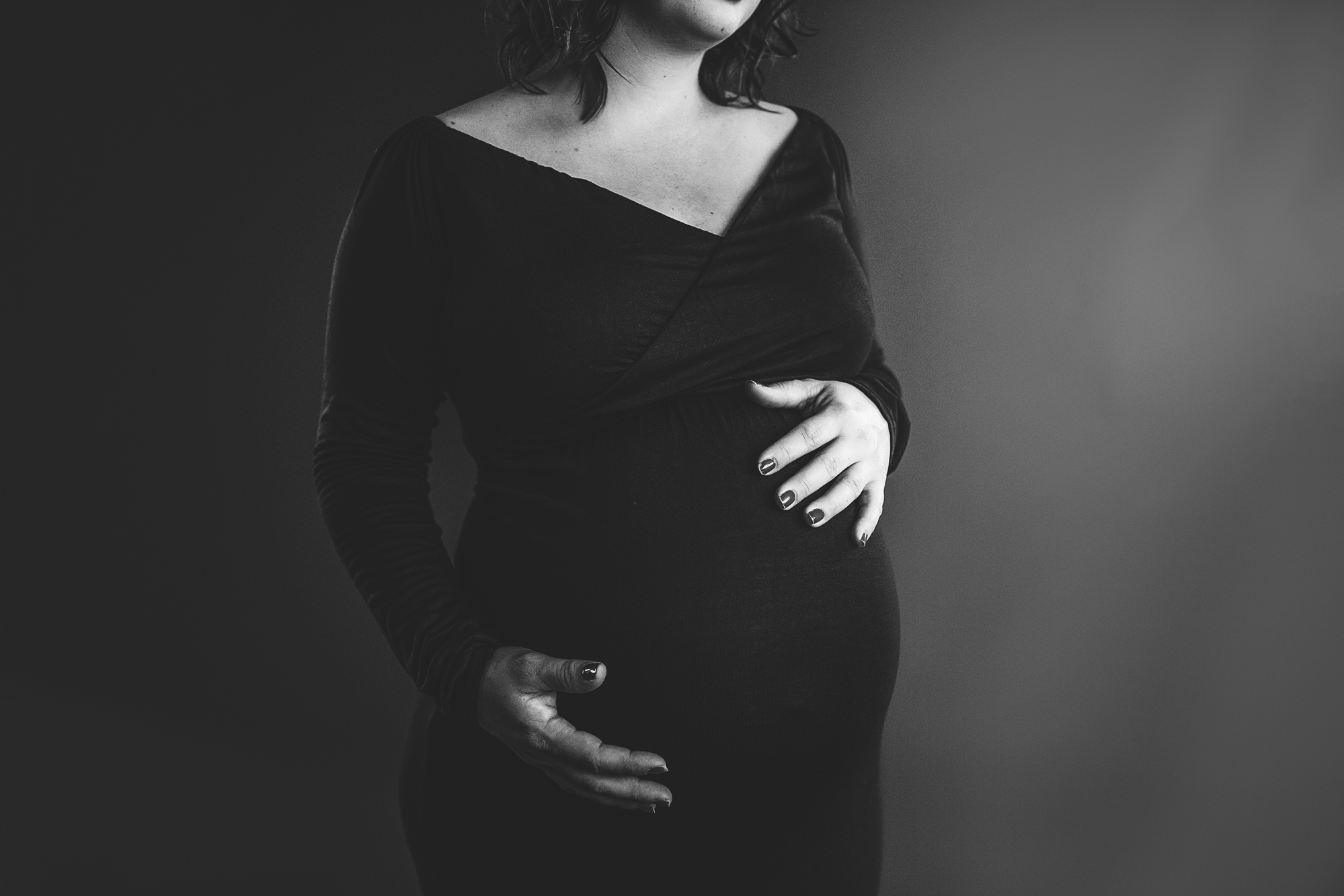 Black and white close-up of a pregnant woman in a dark wrap dress holding her bump