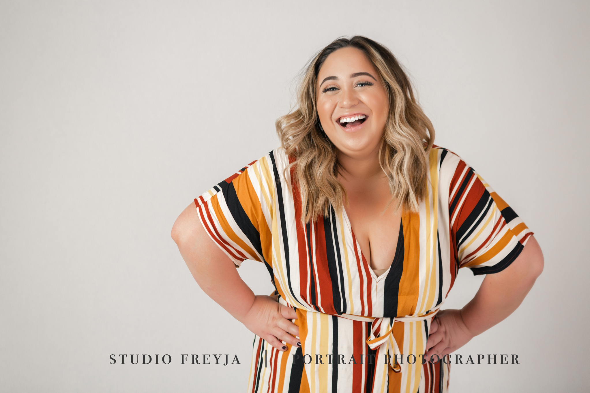 Laughing woman in a striped wrap dress with her hands on her hips