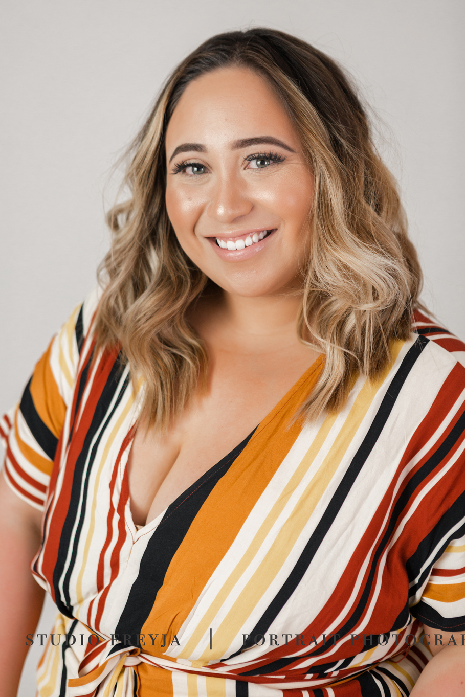 Close-up portrait of a smiling woman with wavy hair in a striped dress
