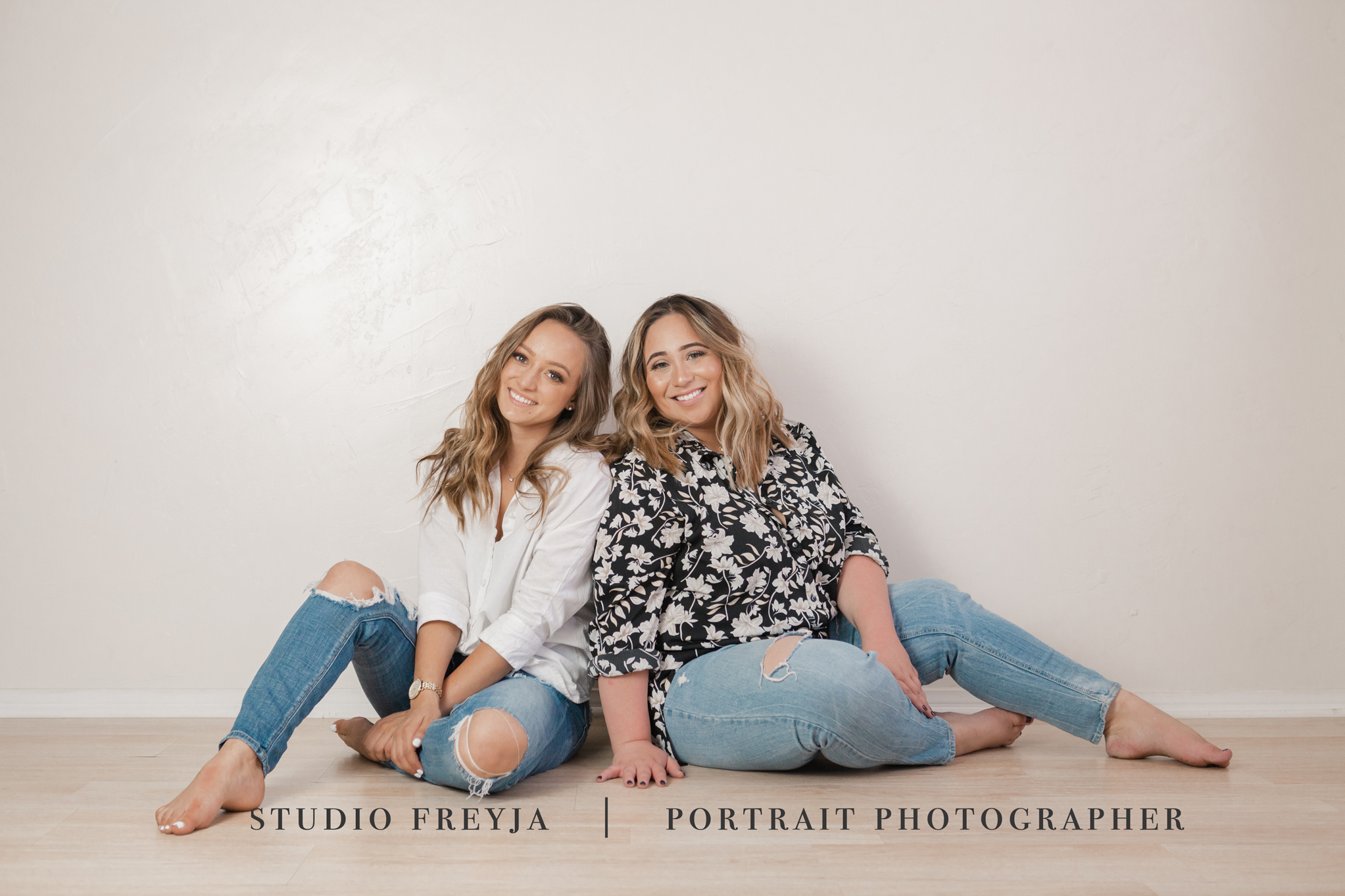 Two business partners sitting on the floor leaning against a white wall, laughing