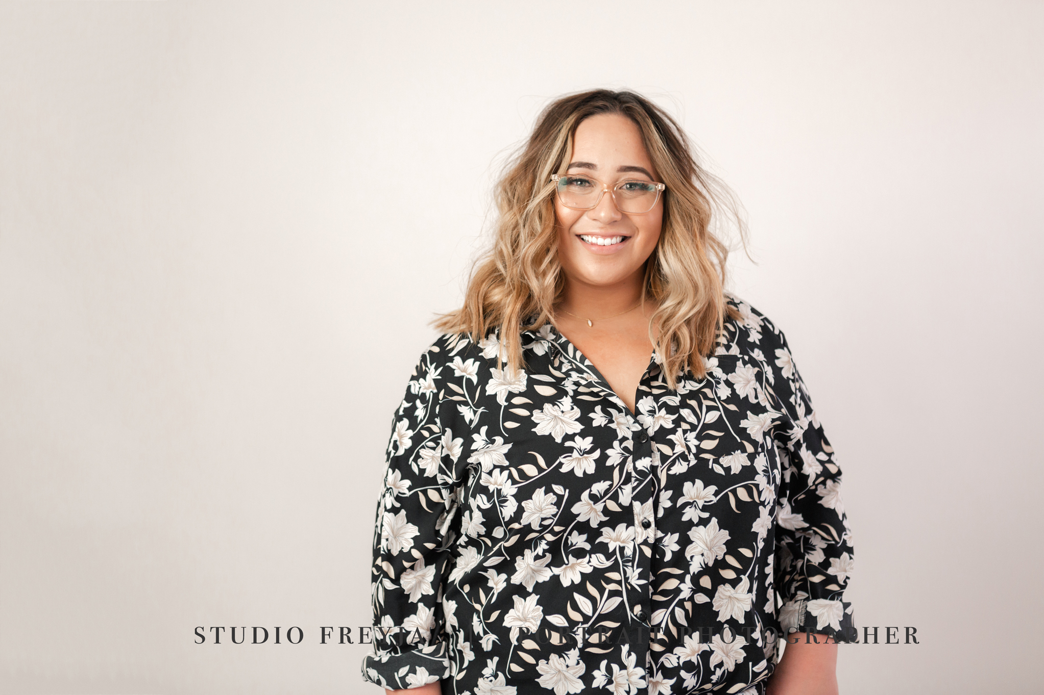 Smiling woman in a black and white floral blouse and glasses against a light wall