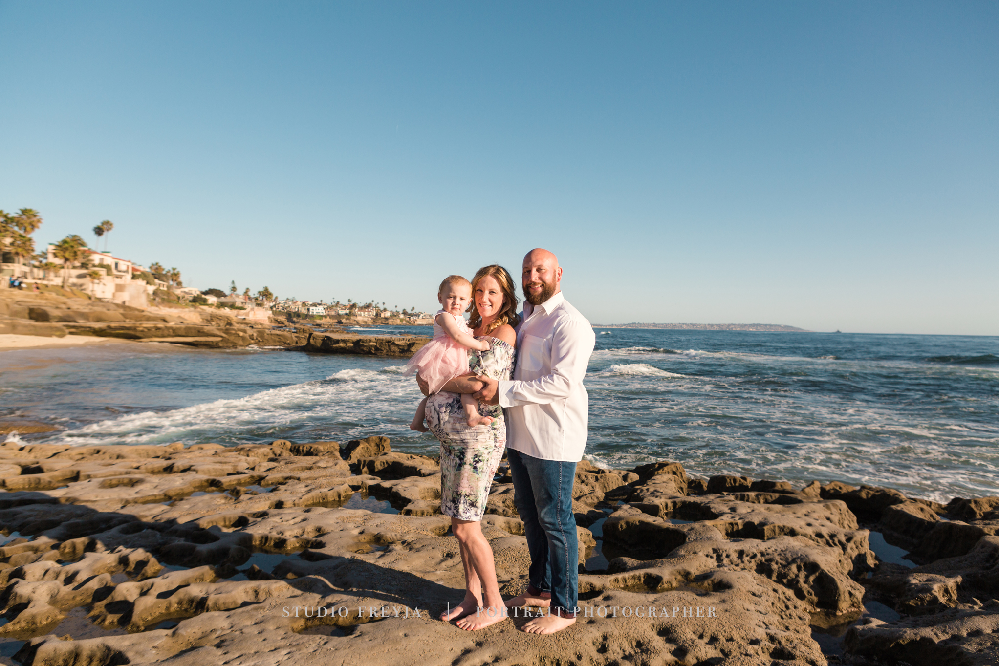 Family of three standing on the rocks at a La Jolla beach, the ocean behind them