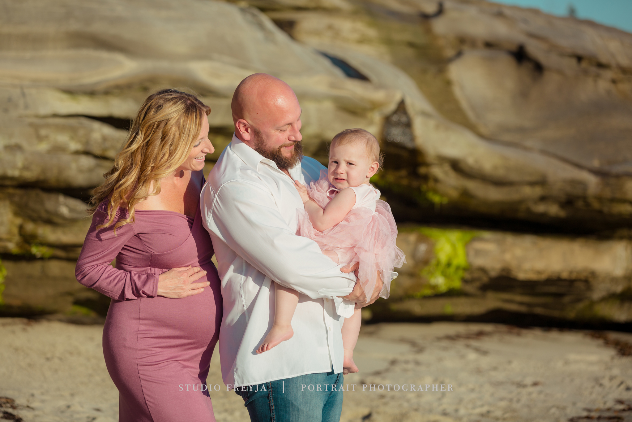 Expectant parents with their toddler daughter in a pink tutu on the beach