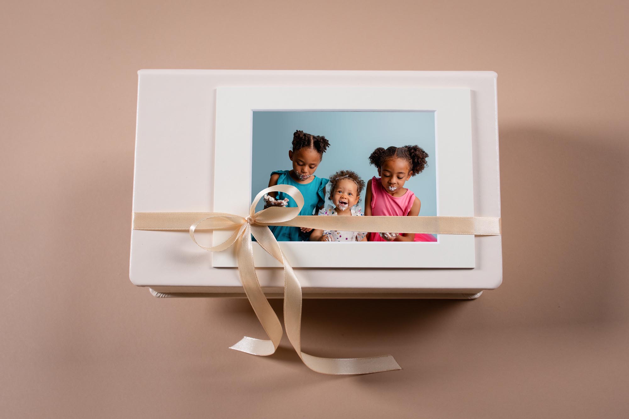 White keepsake box tied with a ribbon holding a matted portrait of three young siblings